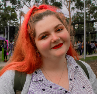 A young female appearing person with long colourful hair smiling at camera. 