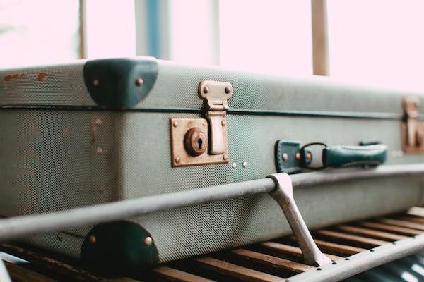 An old grey suitcase with  gold coloured snap closures. It is sitting on a luggage rack. 