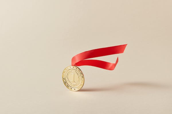 A gold medal with a windblown red ribbon above it. 