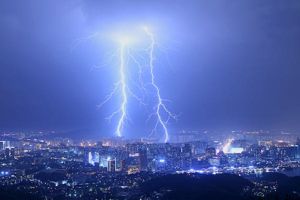 2 big bolts of lightning are flashing down towards a city against a dark blue sky. 