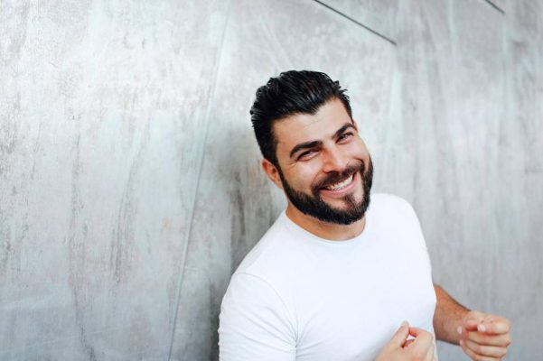 Kyriakos has a big smile, short dark hair and a beard and is wearing a white tshirt.