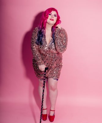 Zoe has pink and purple hair and is wearing a pink sequined dress and holding a walking stick. 