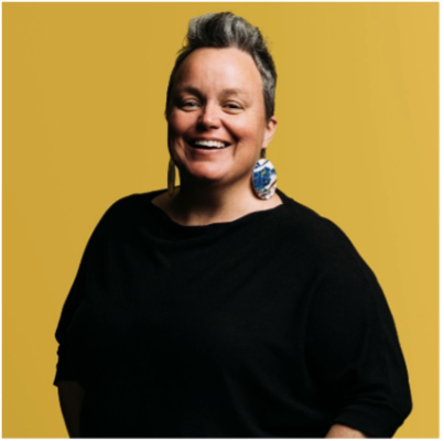 Clare has upswept short hair and is wearing large blue and white earrings and a black top. She has a big smile.