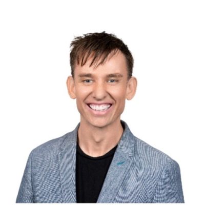 Wayne has a big smile and short dark hair with a fringe. He is wearing a blue linen material jacket.